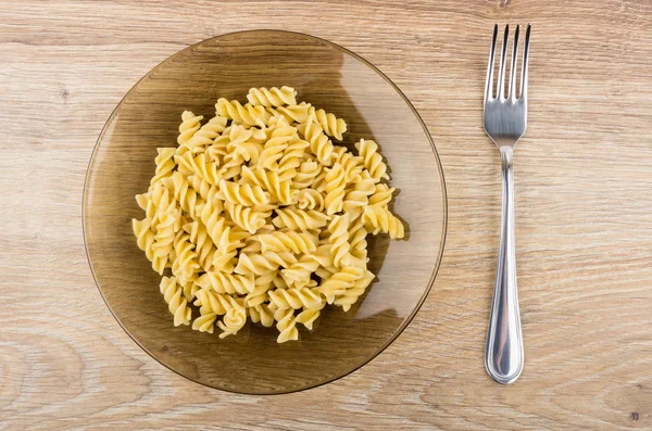 Boiled pasta in transparent brown plate and fork on table