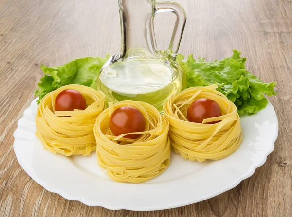 Dish with vegetable oil, pasta tagliatelle and  on wooden table