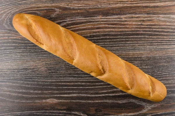 Long loaf of bread on dark wooden table