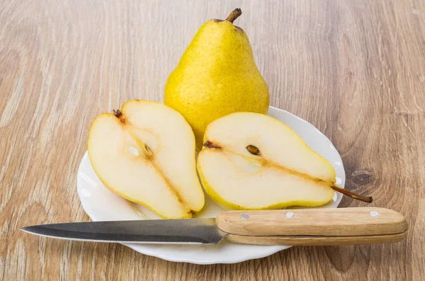 Whole yellow pear, halves of pear and knife in plate