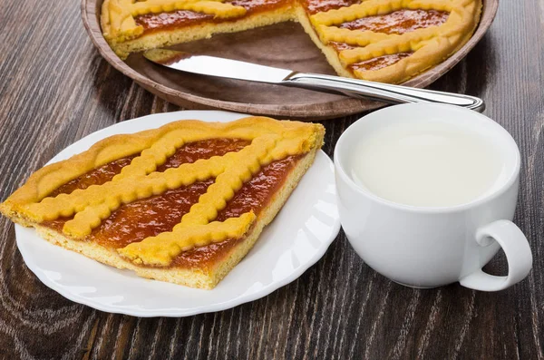 Piece of pie with apricot jam in plate, milk