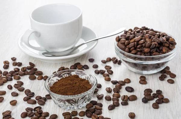 Bowls with ground coffee, coffee beans, empty cup, spoon on wooden table