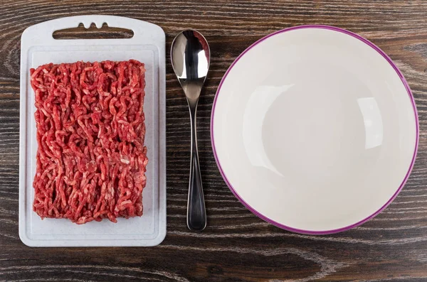 Beef mince on plastic cutting board, empty bowl, spoon
