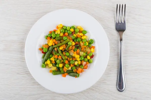 Vegetable mix in plate and fork on wooden table