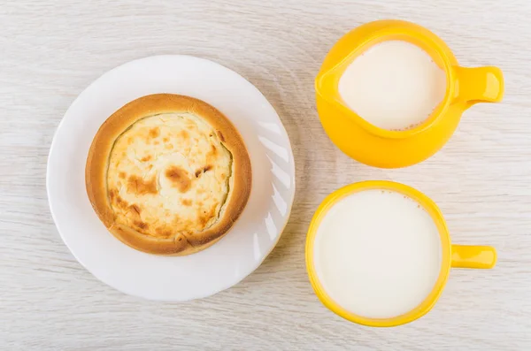 Pie with cottage cheese, jug of milk, milk in cup on wooden table. Top view