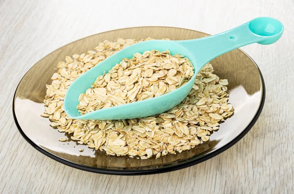 Blue spoon with oat flakes in brown plate on wooden table