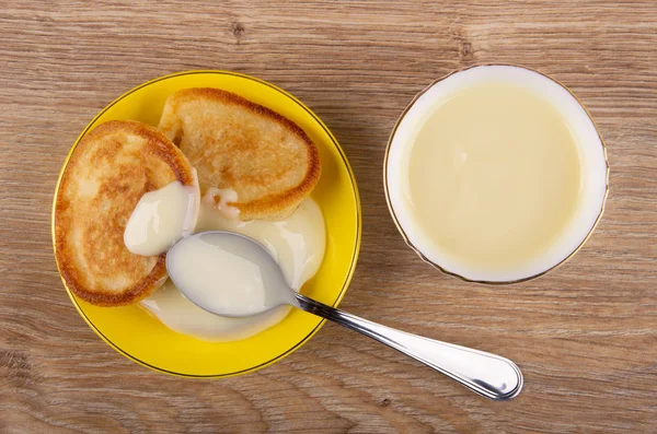 Condensed milk in spoon, pancakes in saucer, bowl with condensed