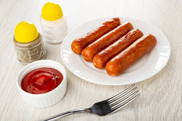 Pepper shaker, salt shaker, bowl with ketchup, fried sausages in