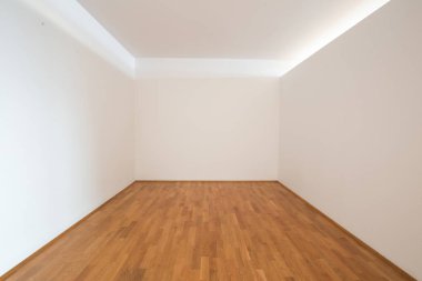 Ahşap döşemeleri ve boş beyaz duvarları olan boş bir oturma odası.