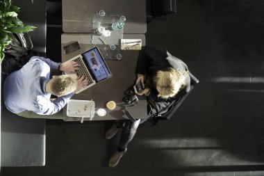 Bir kafede dizüstü bilgisayar ve akıllı telefon kullanan genç bir çiftin gerçek görüntüsü.