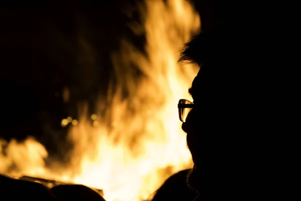 夜になると眼鏡をかけた男がたき火に向かってシルエットになった — ストック写真