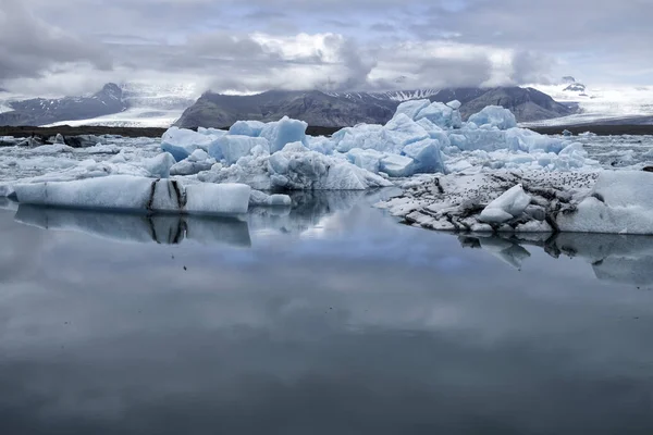 夏にアイスランド南東部の氷河ラグーンに浮かぶ青い氷山 背景にコピースペースと山と氷河がある前景の青い水 ストックフォト