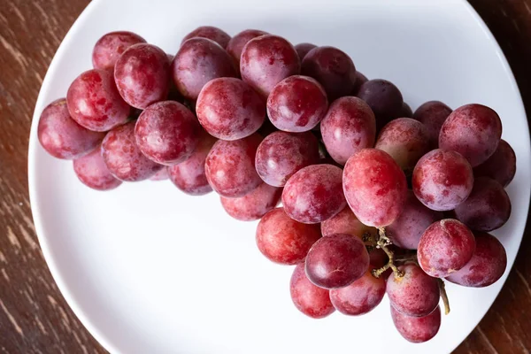 Bagas de uva maduras vermelhas em um prato branco na mesa — Fotografia de Stock