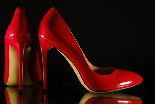 Patent leather shiny female red stilettos on a black background — 图库照片