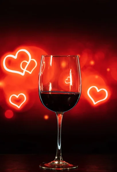 Verre de vin sur une table sur un fond noir-rouge avec des cœurs — Photo
