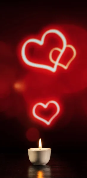 Small candle on the table on a red background with hearts — Stock Photo, Image