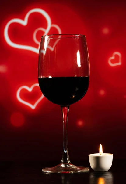 Verre de vin et une petite bougie sur la table sur un fond rouge — Photo