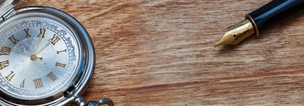 Ручка и карманные часы на деревянном столе — стоковое фото