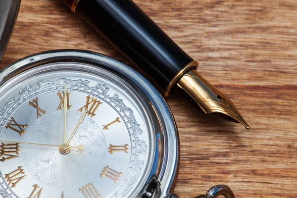 Estilográfica y reloj de bolsillo en una mesa de madera — Foto de Stock