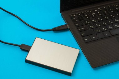 USB üzerindeki harici bir sabit diske bağlı dizüstü bilgisayarı mavi bir arkaplanda aç