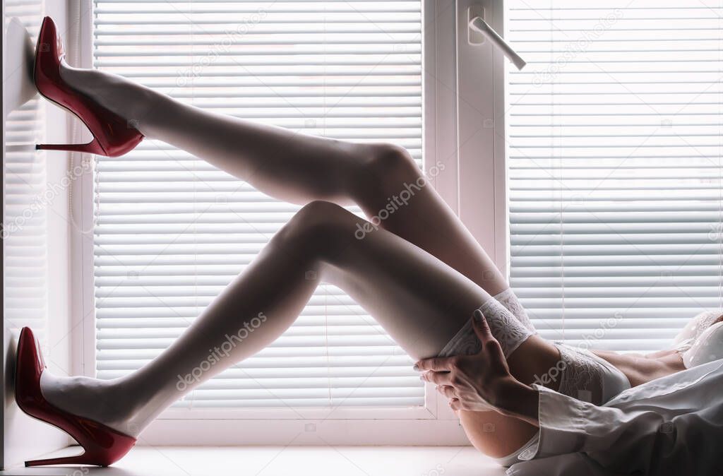 beautiful female legs in red high-heeled shoes on the windowsill near the windo
