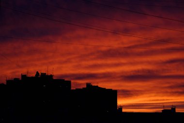 Güzel kırmızı gökyüzü antenli evlerin çatılarının siluetlerinin üzerinde