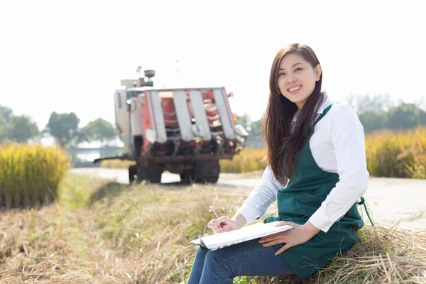 Mulher agrônomo no campo de cereais com colheitadeira — Fotografia de Stock
