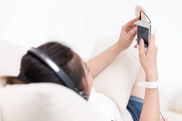 Kvinna på sängen lyssnar musik med mobiltelefon — Stockfoto