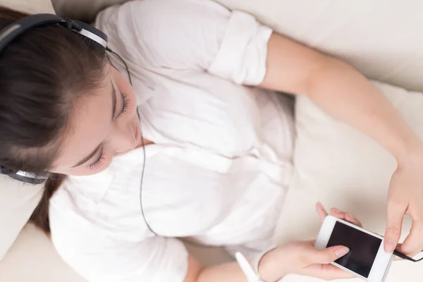 Kvinna på sängen lyssnar musik med mobiltelefon — Stockfoto