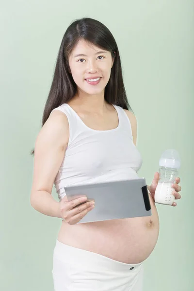 妊娠中の女性は、タブレットとミルクの瓶を保持しています。 — ストック写真