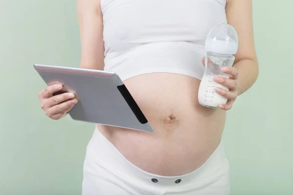 Pregnant woman holds tablet and bottle with milk — Stock Photo, Image