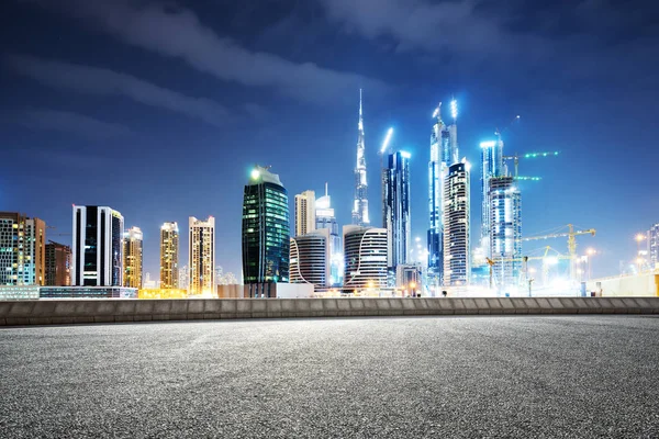 blurry empty asphalt road and modern buildings in midtown of Dubai in cloud sky at night