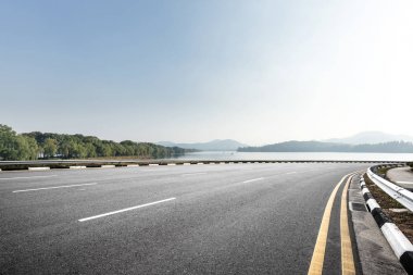Mavi gökyüzü güneşli güzel göl yakınındaki boş asfalt yol