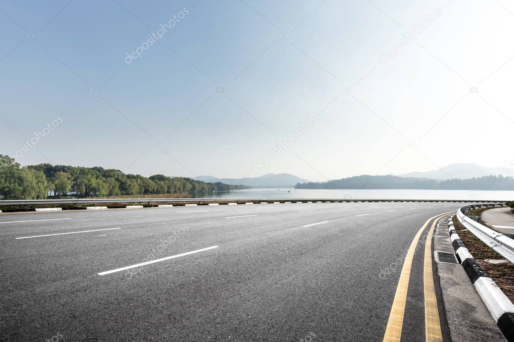 empty asphalt road near beautiful lake in blue sunny sky