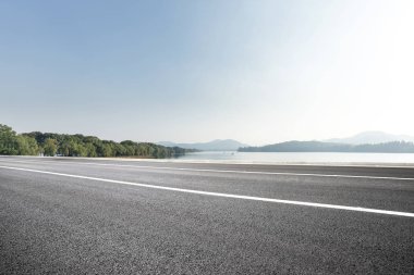 Mavi gökyüzü güneşli güzel göl yakınındaki boş asfalt yol