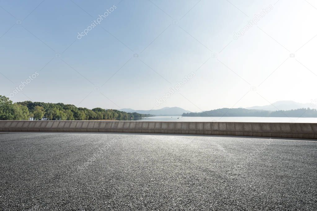 empty asphalt road near beautiful lake in blue sunny sky