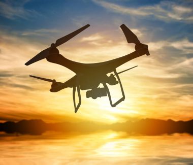 Bir gün batımı gökte uçan dijital fotoğraf makinesi ile bir dron silüeti