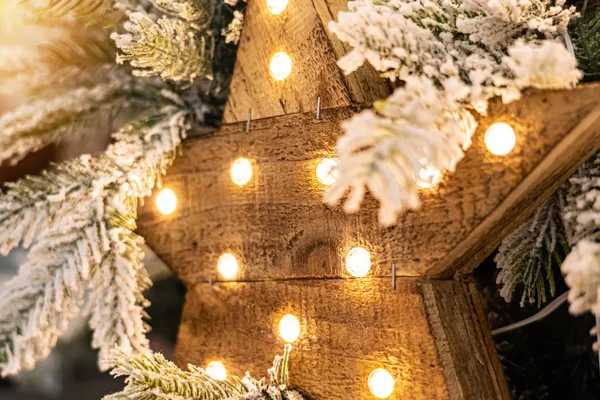 Красива декоративна дерев'яна зірка з лампами, що висять на соснових гілках зі святковим фоном — стокове фото