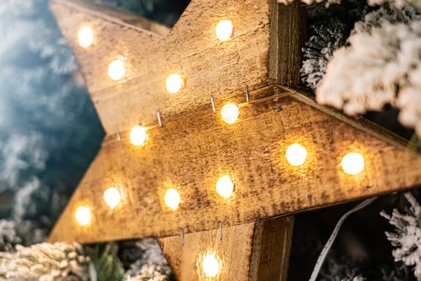 Estrela de madeira decorativa com lâmpadas penduradas em galhos de pinho com fundo festivo — Fotografia de Stock