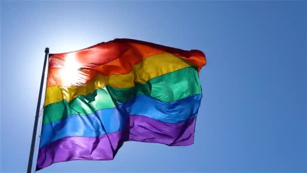 Bandeira do arco-íris acenando ao vento no céu azul — Vídeo de Stock