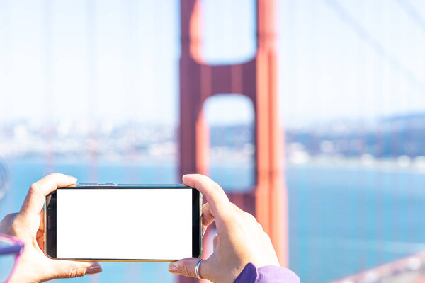 Female hands taking photo on smart phone in front of Golden Gate, SF. Mockup