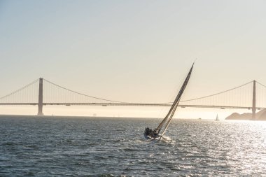 Gün batımında San Francisco körfezinde güzel bir yat, ufukta Golden Gate köprüsü