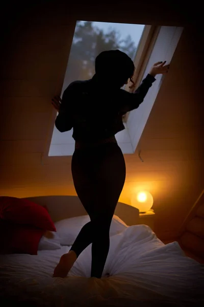 Jeune femme dans le capot posant contre la fenêtre dans la chambre sombre — Photo