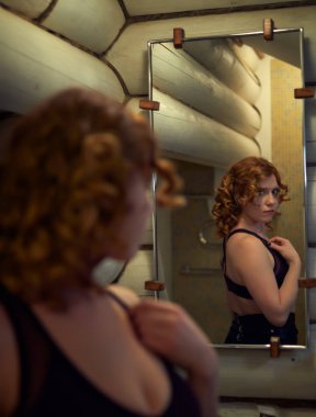 Kızıl saçlı genç kadın kendini ba aynaya bakarak