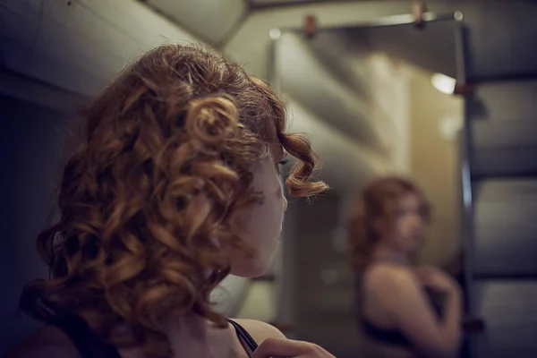 Vörös hajú fiatal nő nézi magát a tükörben, a ba — Stock Fotó