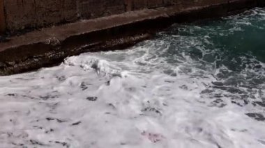 Deniz dalgaları kıyı dalgalarında kırılır ve kayalık bir plaja düşer.