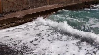 Deniz dalgaları kıyı dalgalarında kırılır ve kayalık bir plaja düşer.