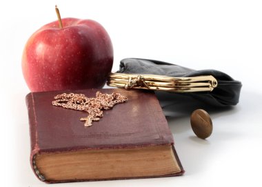 Metal bir para çantasının yanında olgun bir elma ve altın haçlı bir dini kitap.