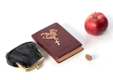 Metal bir para çantasının yanında olgun bir elma ve altın haçlı bir dini kitap.