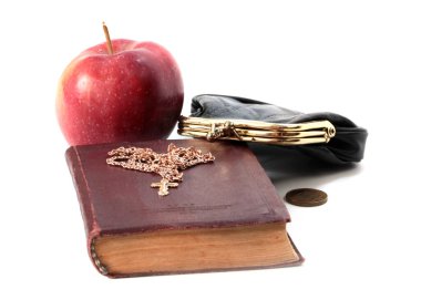 Metal bir para çantasının yanında olgun bir elma ve altın haçlı bir dini kitap.